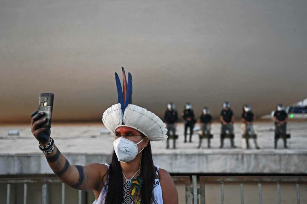 Au Brésil : Une indigène prend un selfie devant la police antiémeute, lors d’une manifestation devant le bâtiment de la Cour suprême, à Brasilia, le 24 août 2021. CARL DE SOUZA / AFP